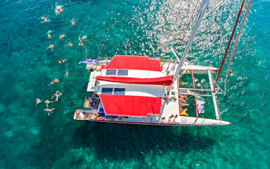 Aerial view of a catamaran cruise with swimmers in Santorini's clear waters.