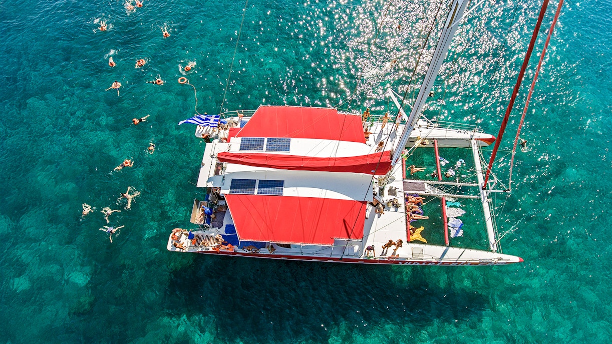 Aerial view of a catamaran cruise with swimmers in Santorini, Greece.