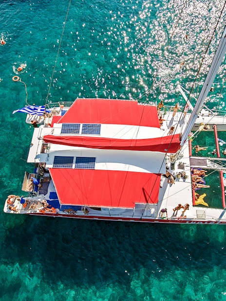 Aerial view of a catamaran cruise with swimmers in Santorini's clear waters.