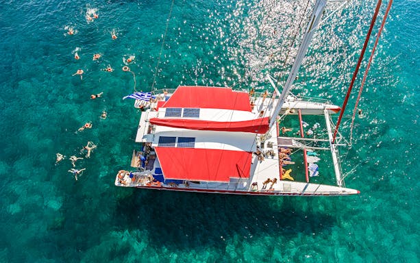 Aerial view of a catamaran cruise with swimmers in Santorini's clear waters.