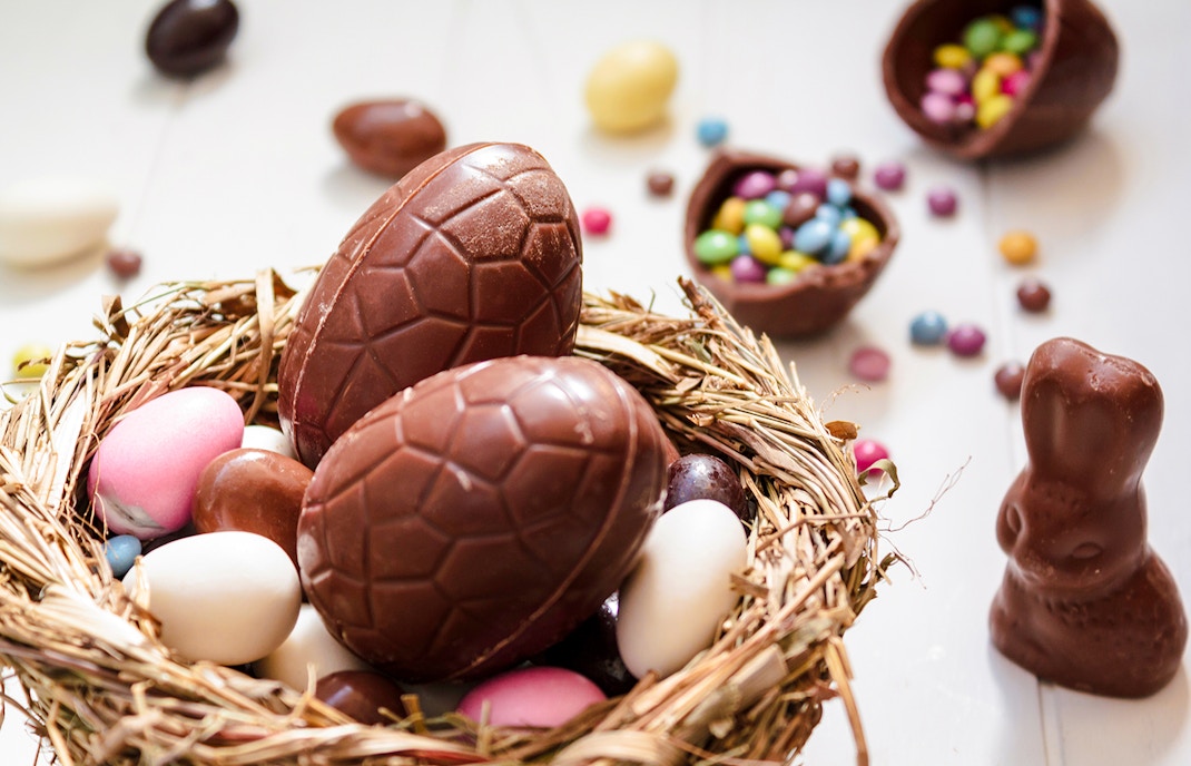 Chocolate eggs and Easter almonds in nest with chocolate bunny on white wooden table.