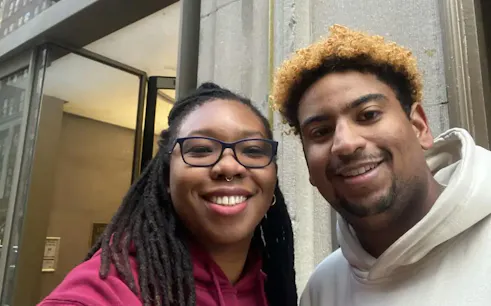 Two people smiling outside a building in New York during a self-guided city exploration game.