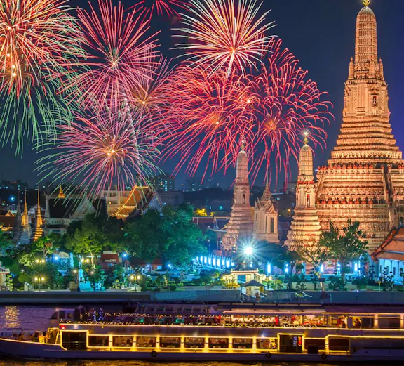 Wat Arun illuminated with fireworks and a cruise ship on the Chao Phraya River, Bangkok, Thailand.