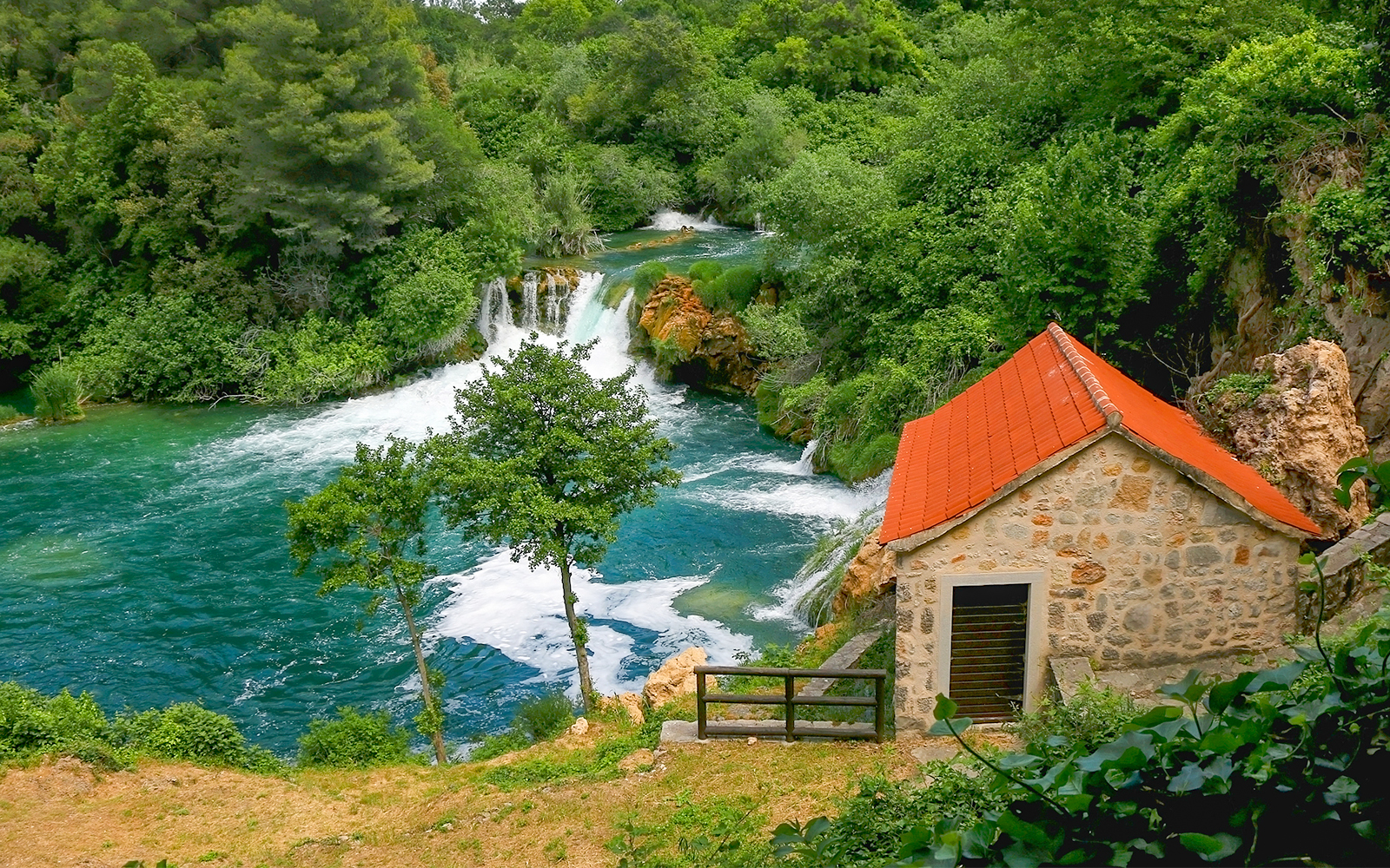 Waterfall and stone house at Krka National Park, Croatia, surrounded by lush greenery.