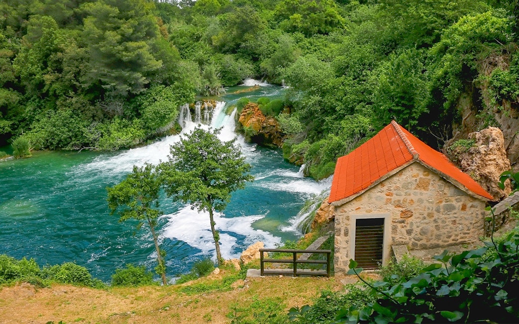 Waterfall and stone house at Krka National Park, Croatia, surrounded by lush greenery.