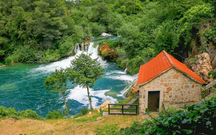 Waterfall and stone house at Krka National Park, Croatia, surrounded by lush greenery.