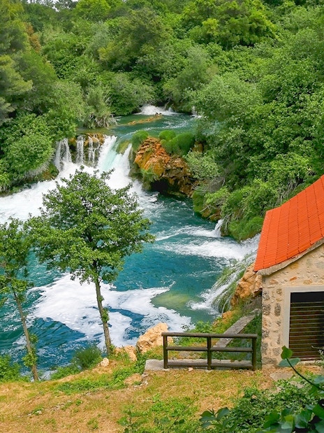 Waterfall and stone house at Krka National Park, Croatia, surrounded by lush greenery.