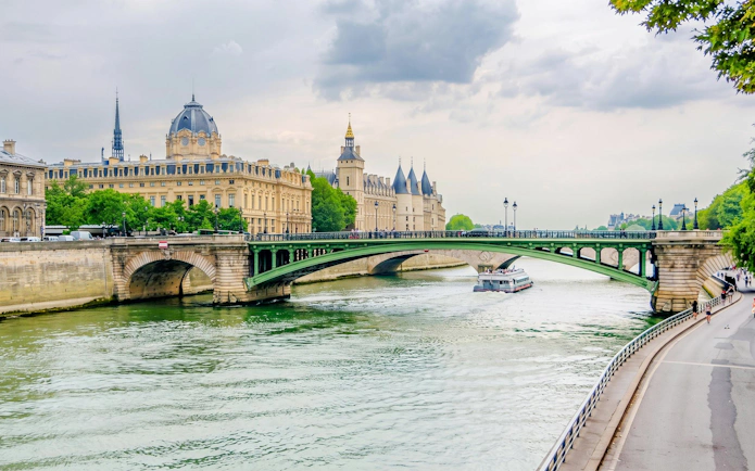 Seine River cruise boat passing under a bridge in Paris near historic buildings.