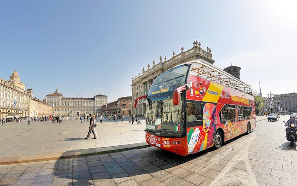 Open-top tour bus in Piazza Castello, Turin, with historic buildings in the background.