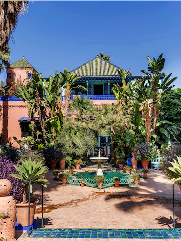 Jardin Majorelle courtyard with fountain, lush greenery, and vibrant blue building in Marrakech, Morocco.
