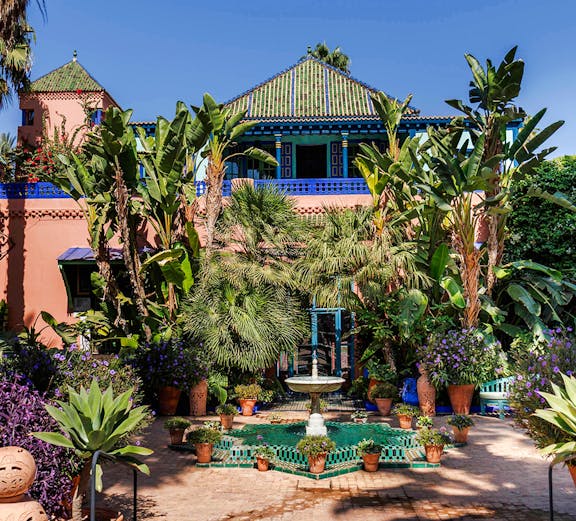Jardin Majorelle courtyard with fountain, lush greenery, and vibrant blue building in Marrakech, Morocco.