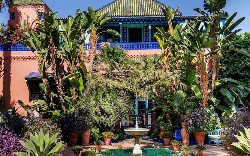 Jardin Majorelle courtyard with fountain, lush greenery, and vibrant blue building in Marrakech, Morocco.