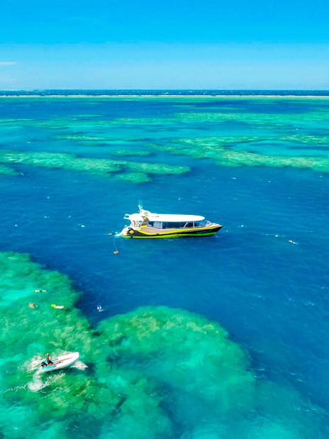 Boat sailing over clear waters of Whitsundays Islands with snorkelers exploring the reef.