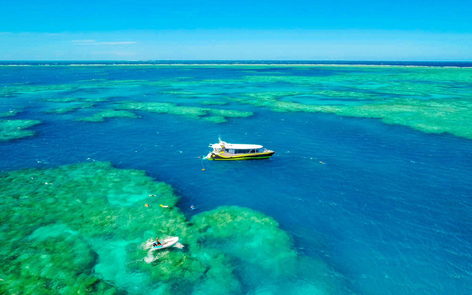 Boat sailing over clear waters of Whitsundays Islands with snorkelers exploring the reef.