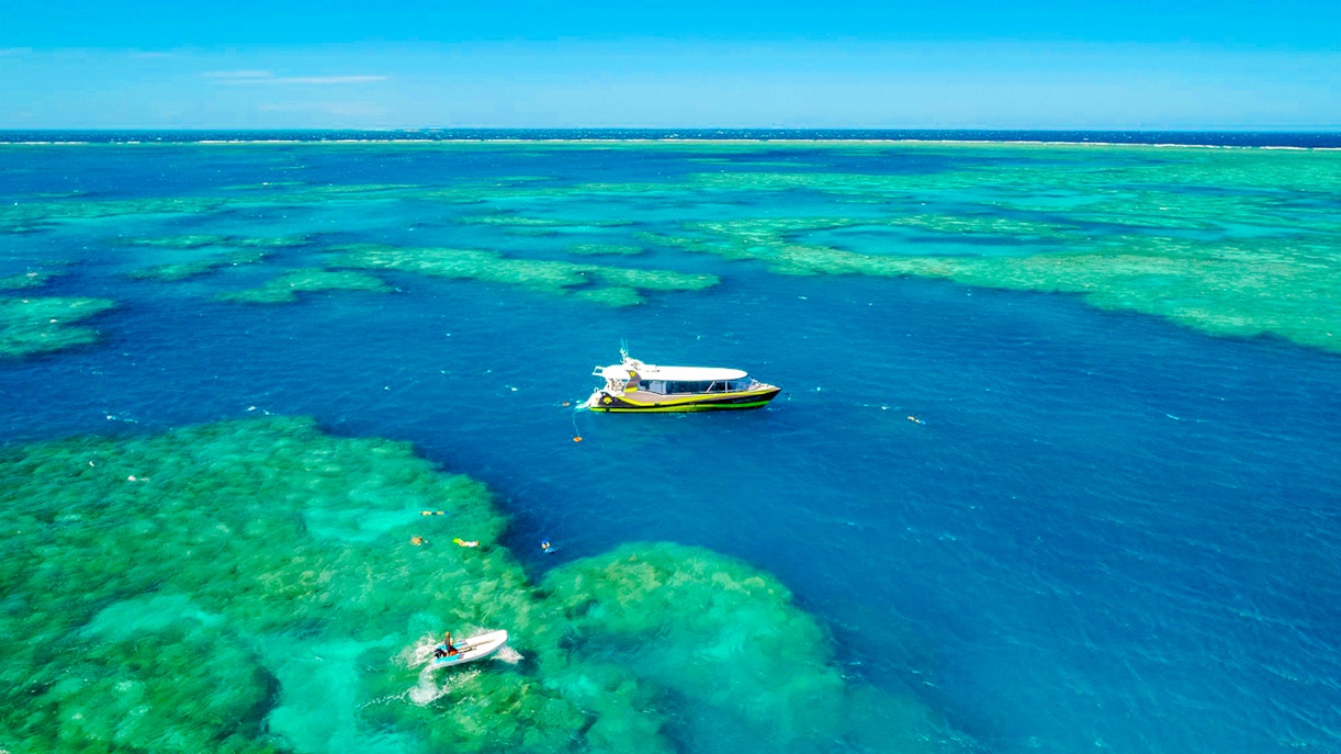 Boat sailing over clear waters of Whitsundays Islands with snorkelers exploring the reef.