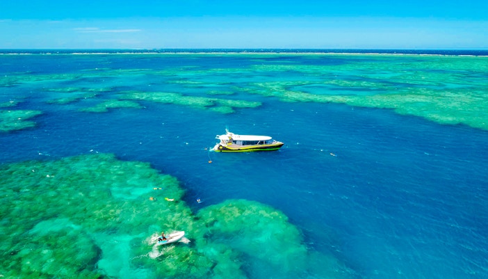 Boat sailing over clear waters of Whitsundays Islands with snorkelers exploring the reef.