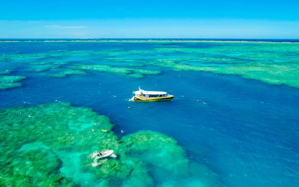 Boat sailing over clear waters of Whitsundays Islands with snorkelers exploring the reef.