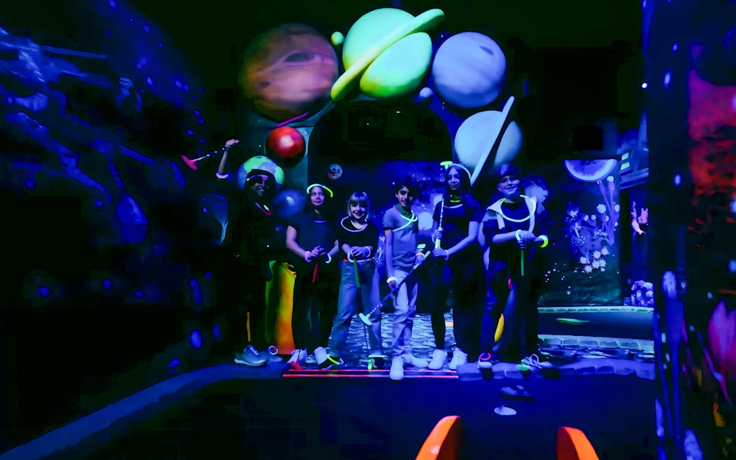 Guests playing blacklight mini golf with glowing planets in the background.