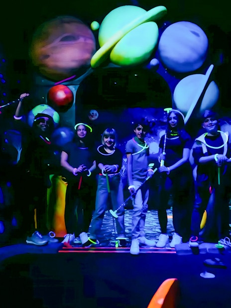 Guests playing blacklight mini golf with glowing planets in the background.
