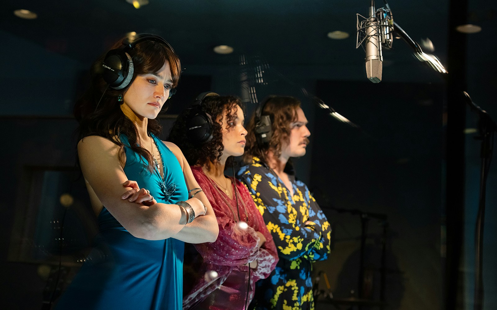 Three people wearing headphones in a recording studio with a microphone, related to stereophonic.