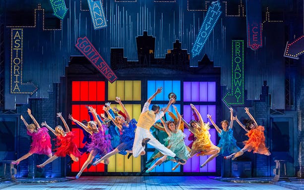 Performers dancing energetically on stage in colorful costumes during Singin’ in the Rain show.