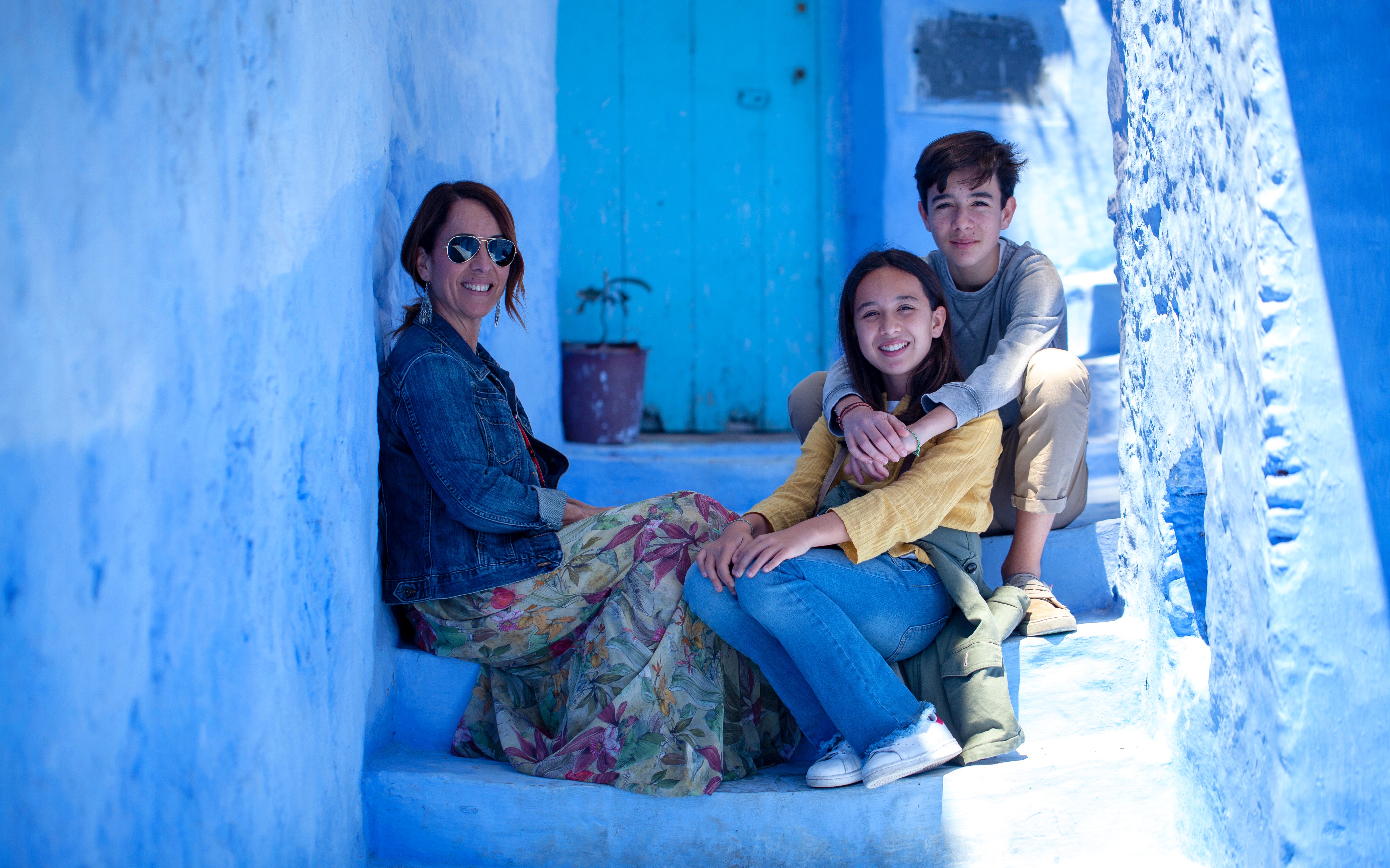 Tourist family sitting on blue steps in Chefchaouen, Morocco.