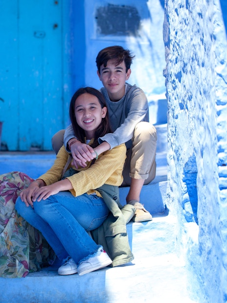 Tourist family sitting on blue steps in Chefchaouen, Morocco.