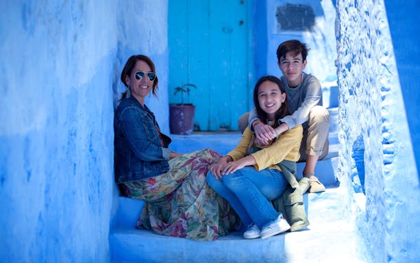 Tourist family sitting on blue steps in Chefchaouen, Morocco.
