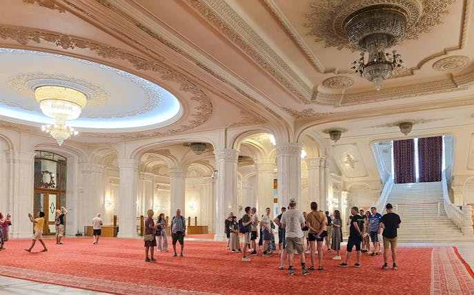 Guided tour group in the grand hall of the Palace of Parliament, near the staircase.