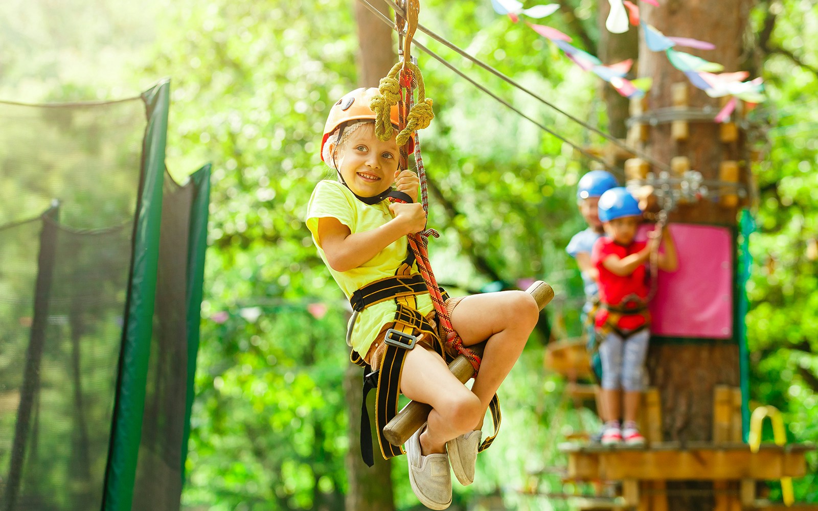 Brave young girl in helmet climbs on tree tops in zoo park on summer holidays
