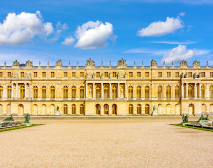 Palace of Versailles facade with statues and blue sky.