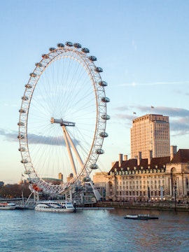 London Eye overlooking the Thames River with nearby historic buildings.