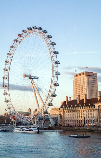 London Eye overlooking the Thames River with nearby historic buildings.