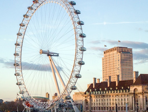 London Eye overlooking the Thames River with nearby historic buildings.