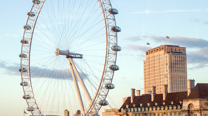 London Eye overlooking the Thames River with nearby historic buildings.