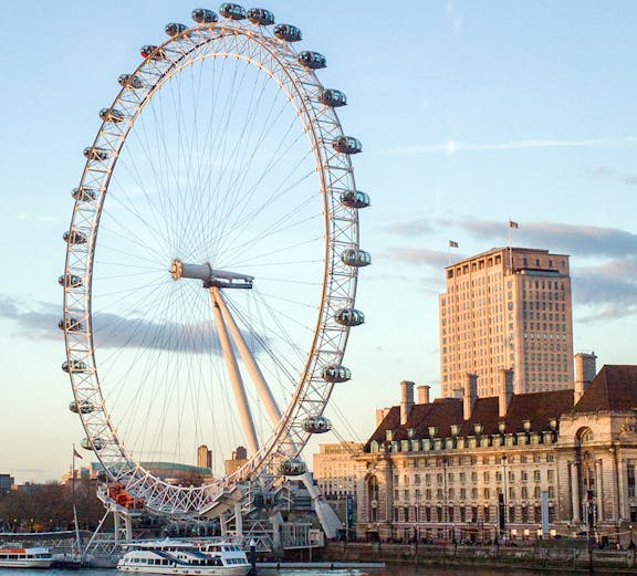 London Eye overlooking the Thames River with nearby historic buildings.