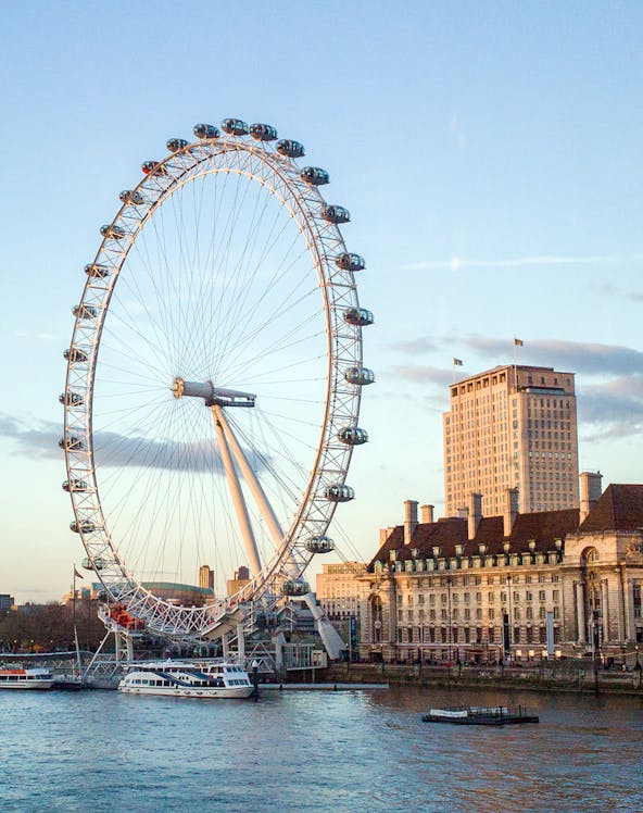 London Eye overlooking the Thames River with nearby historic buildings.