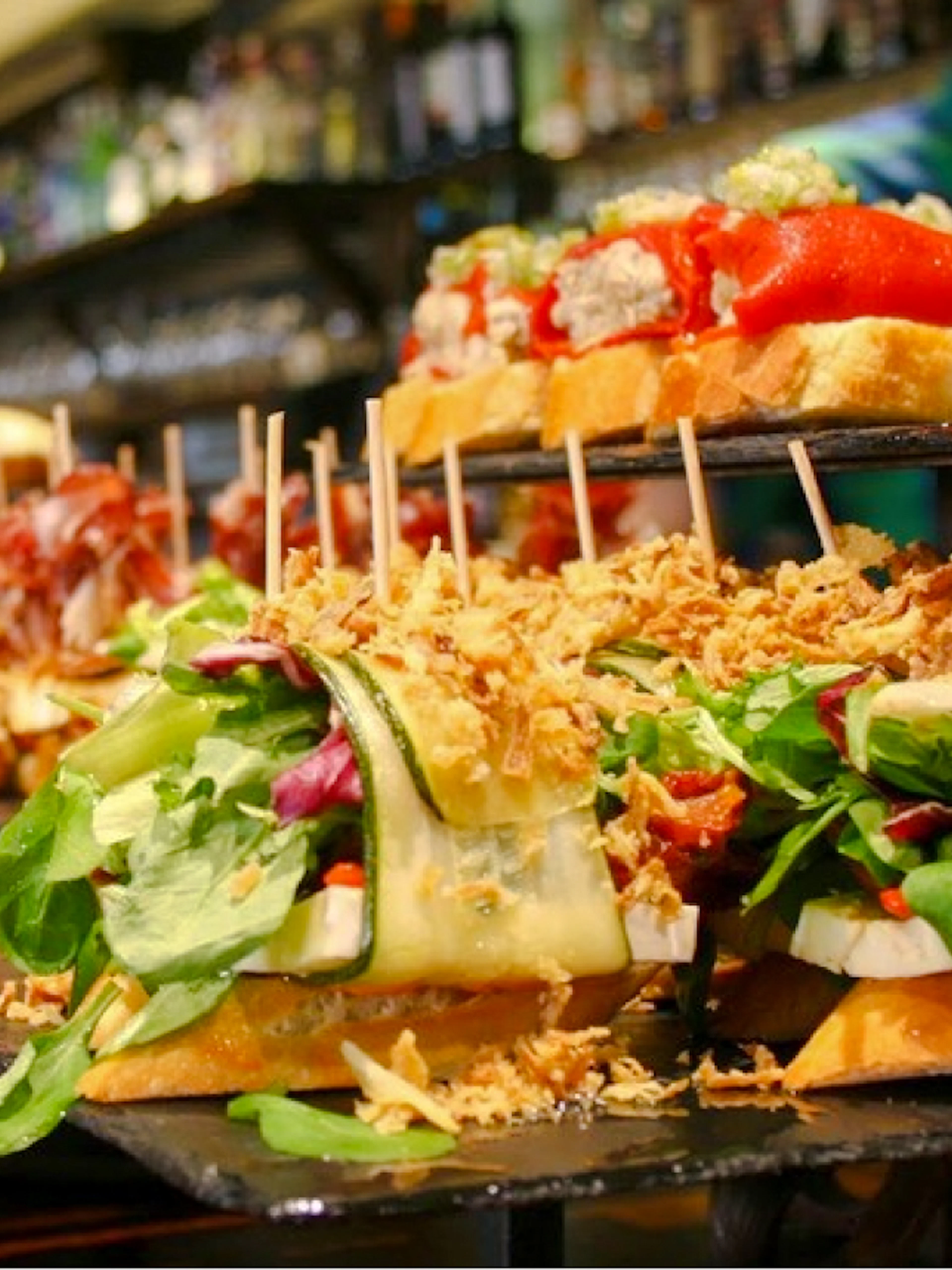 Pintxos assortment at a bar in San Sebastian, featuring fresh vegetables and cured meats.