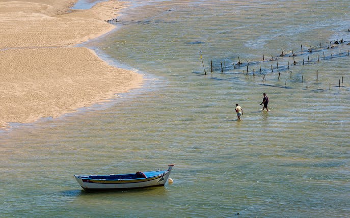 Boat and people wading in shallow water during 4 Islands Guided Tour in Faro.