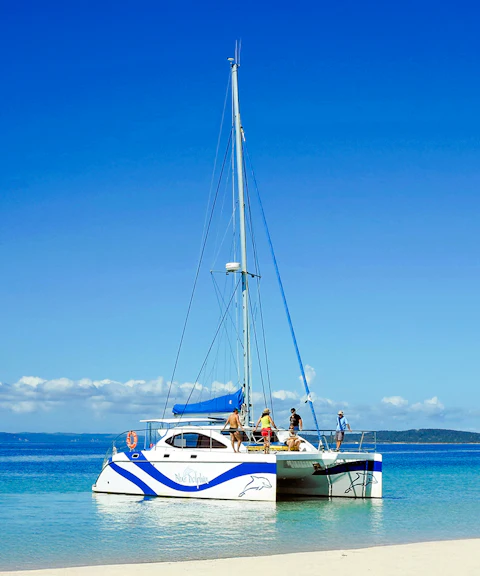 Catamaran sailing near Fraser Island, K'gari with people on deck, clear blue water.