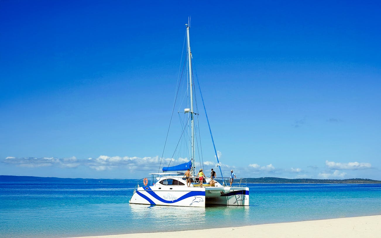 Catamaran sailing near Fraser Island, K'gari with people on deck, clear blue water.