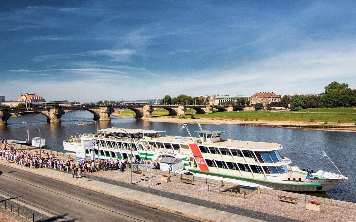 Cruise ship docked on the Elbe River in Dresden with Augustus Bridge in the background.