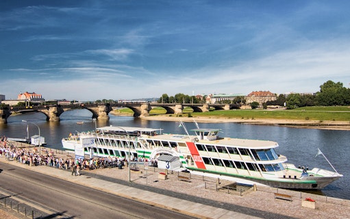 Cruise ship docked on the Elbe River in Dresden with Augustus Bridge in the background.