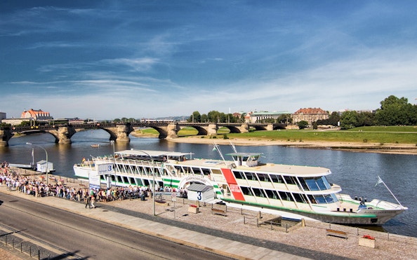 Cruise ship docked on the Elbe River in Dresden with Augustus Bridge in the background.