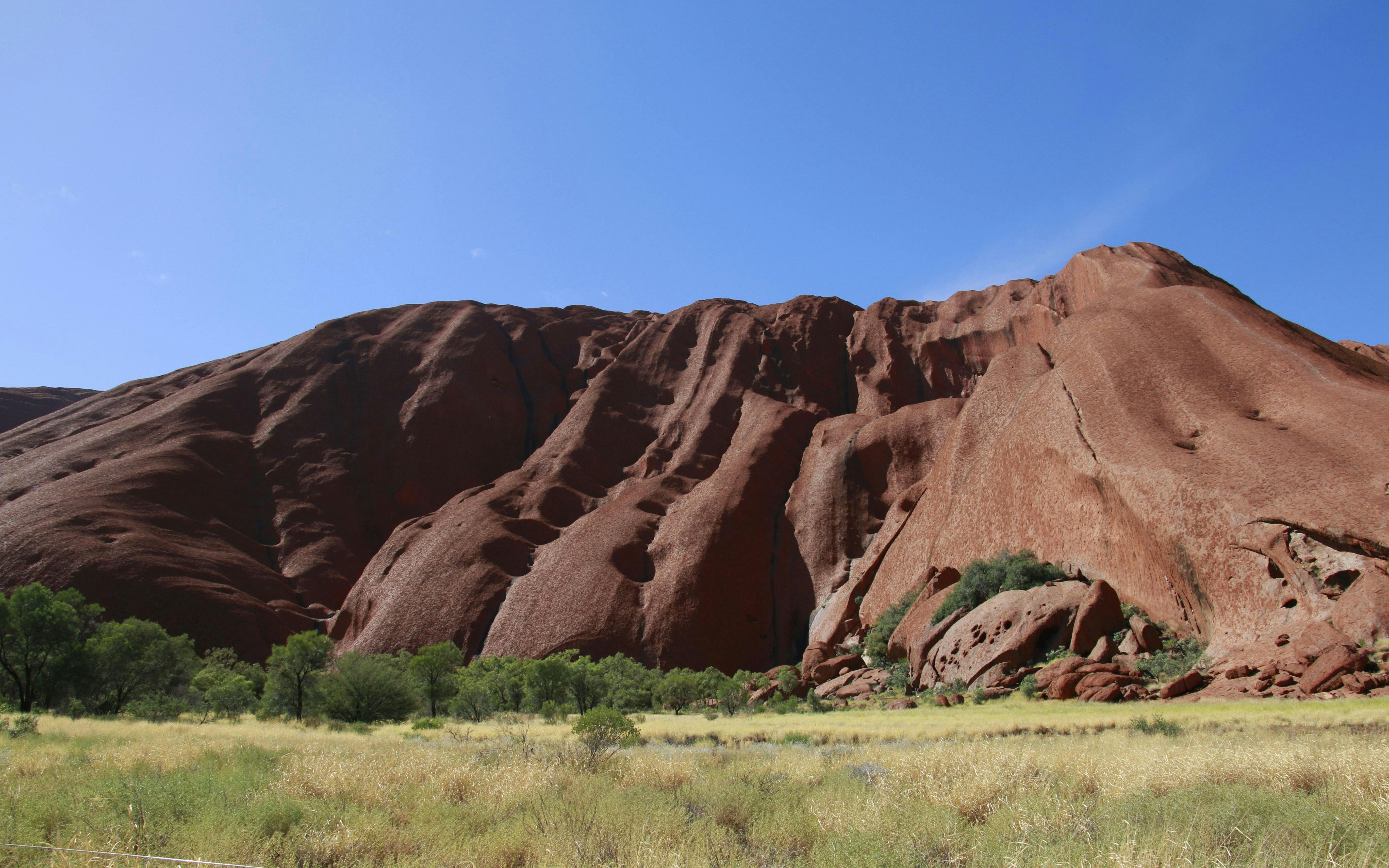 Uluru rock formation under clear blue sky during sunset tour in Australia.
