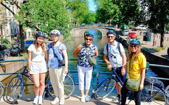 Group of cyclists on a bridge over a canal during Amsterdam City Highlights Bike Tour.
