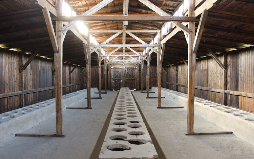 Interior of Auschwitz I barracks showing wooden beams and concrete latrines.
