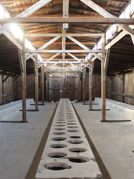 Interior of Auschwitz I barracks showing wooden beams and concrete latrines.