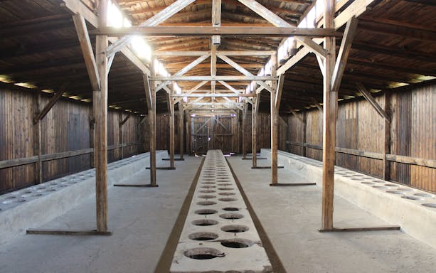 Interior of Auschwitz I barracks showing wooden beams and concrete latrines.