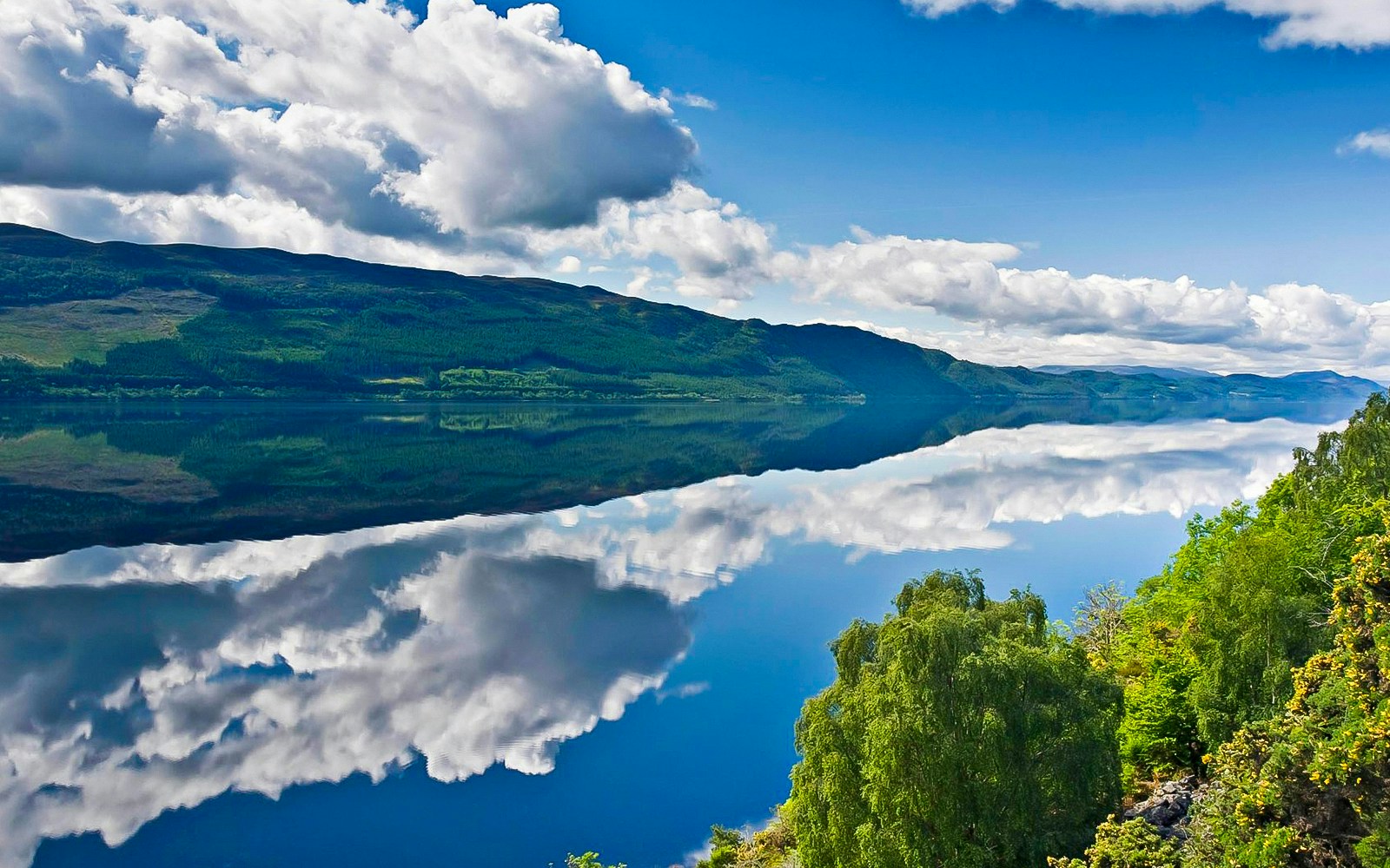 Loch Ness River with clear reflections of clouds and surrounding green hills.